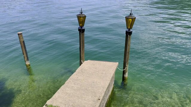 Lamp on Pier on Alpine Lake Lugano and Mountain in a Sunny Day in Melide and Bissone in Ticino, Switzerland.