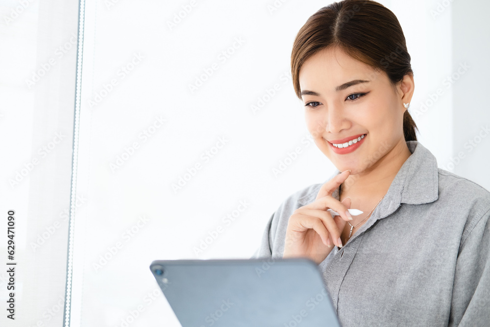 Wall mural young asian businesswoman is happy to work at the modern office using a tablet. copy space