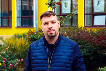 Young caucasian 34 years old man in blue jacket with goatee beard on yellow building. Looking at...