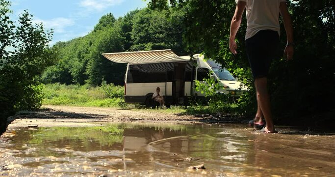 In the  of the forest, a couple living the caravan life sits in their chairs by the stream, savoring the beauty of nature 