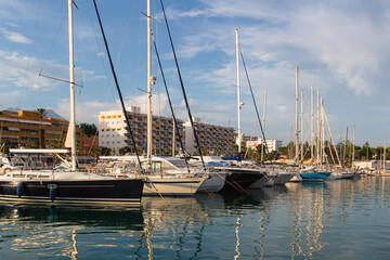 Sport yachts in the marina at sunset. Sailing yacht on the resort's pier in a backdrop of tourist hotels. Anchorage on the sea in a yacht club. Rigging ropes and metal cables on the bow of a sailboat