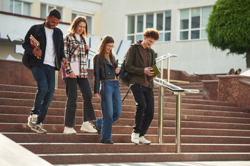 Obraz premium Going down the stairs. Four young students in casual clothes are together outdoors