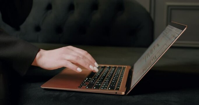 Schoolgirl with manicured nude manicure typing and surfing internet on laptop in modern black office. College student doing her higher studies at a distance. Woman working on the computer. Close-up