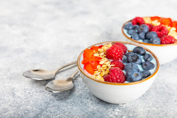 Bowl of granola with yogurt and fresh berries on a texture table. Yogurt berries, acai bowl, spirulina bowl. Healthy food, balanced breakfast. Strawberries, blueberries, kiwi, peach, almonds and chia.
