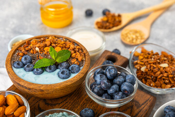Bowl of granola with yogurt and fresh berries on a texture table. Yogurt berries, acai bowl, spirulina bowl. Healthy food, balanced breakfast. Strawberries, blueberries, kiwi, peach, almonds and chia.