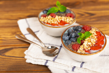 Bowl of granola with yogurt and fresh berries on a texture table. Yogurt berries, acai bowl, spirulina bowl. Healthy food, balanced breakfast. Strawberries, blueberries, kiwi, peach, almonds and chia.
