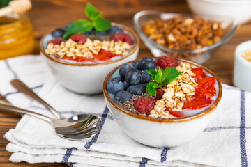 Bowl of granola with yogurt and fresh berries on a texture table. Yogurt berries, acai bowl, spirulina bowl. Healthy food, balanced breakfast. Strawberries, blueberries, kiwi, peach, almonds and chia.