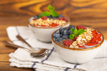 Bowl of granola with yogurt and fresh berries on a texture table. Yogurt berries, acai bowl, spirulina bowl. Healthy food, balanced breakfast. Strawberries, blueberries, kiwi, peach, almonds and chia.