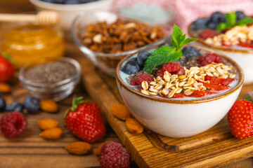 Bowl of granola with yogurt and fresh berries on a texture table. Yogurt berries, acai bowl, spirulina bowl. Healthy food, balanced breakfast. Strawberries, blueberries, kiwi, peach, almonds and chia.