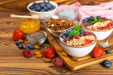 Bowl of granola with yogurt and fresh berries on a texture table. Yogurt berries, acai bowl, spirulina bowl. Healthy food, balanced breakfast. Strawberries, blueberries, kiwi, peach, almonds and chia.