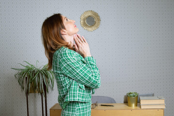 Middle-aged woman folded her hands in prayer in her office. Business woman in a green jacket is...