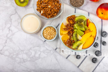 Bowl of granola with yogurt and fresh berries on a texture table. Yogurt berries, acai bowl, spirulina bowl. Healthy food, balanced breakfast. Strawberries, blueberries, kiwi, peach, almonds and chia.