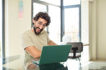 young adult bearded man with a laptop with a big, friendly, carefree smile, looking positive, relaxed and happy, chilling