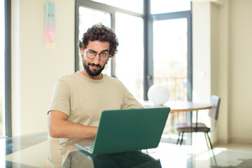 young adult bearded man with a laptop looking proud, confident, cool, cheeky and arrogant, feeling successful