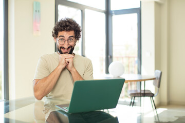 young adult bearded man with a laptop happy and excited, surprised and amazed, giggling with a cute expression