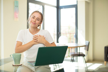 caucasian pretty woman with a laptop feeling romantic, happy and in love, smiling cheerfully and holding hands close to heart