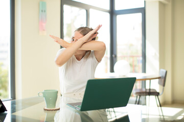 caucasian pretty woman with a laptop covering face with hand and putting other hand up front to...