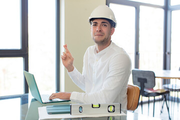 young handsome man crossing fingers and hoping for good luck. architect concept