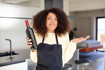 pretty afro black woman shrugging, feeling confused and uncertain. wine bottle concept