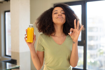 pretty afro black woman feeling happy, showing approval with okay gesture. orange juice concept