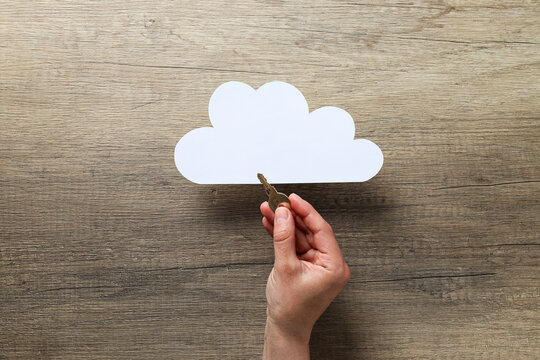 White paper cloud and hand with key on wooden background