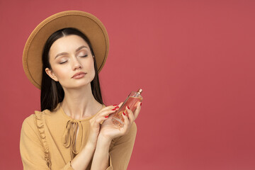 Young woman in hat with perfume bottle on pink background, space for text