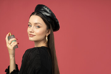 Young woman in beret with perfume bottle on pink background, space for text