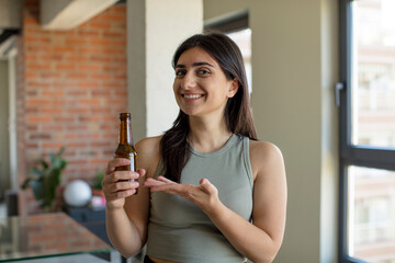 young woman smiling cheerfully, feeling happy and showing a concept. beer bottle