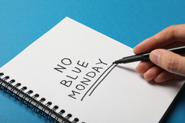 Notepad with text No Blue Monday, marker in hand on blue background