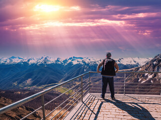 A man tourist stands on an observation deck on a mountain above a valley;