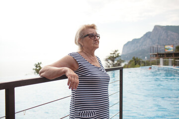 Beautiful old woman in pool against sea. Senior woman dressed swimsuit and enjoy swim in the pool...