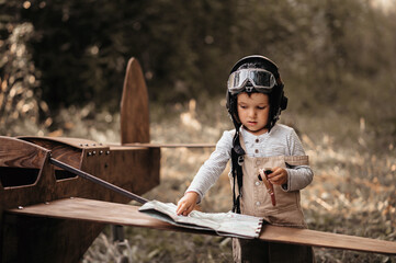A young aviator boy near a homemade airplane in a natural landscape with a compass and a...