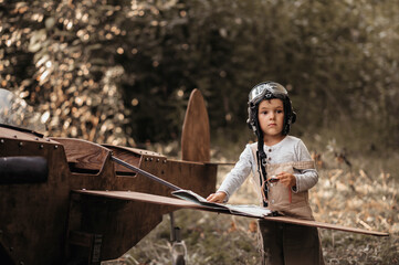 A young aviator boy near a homemade airplane in a natural landscape with a compass and a...