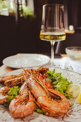 Langoustine with lemon and wine. Seafood close up. Fish dish with glass of wine. Fish restaurant menu. Grilled scampi with salad. Mediterranean mollusk plate. Flat lay photo. Roasted shrimps.