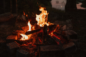 A bonfire in close-up, flames, charred pieces of logs and ashes in the open air against the landscape. Camping.