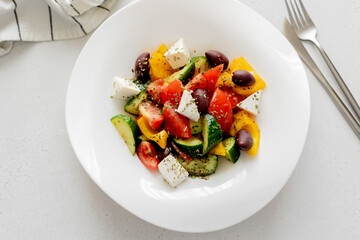 Greek vegetable salad with feta cheese and cutlery on light table background. Top view