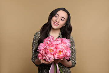 Beautiful young woman with bouquet of pink peonies on light brown background