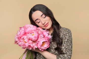 Fototapeta premium Beautiful young woman with bouquet of pink peonies on light brown background