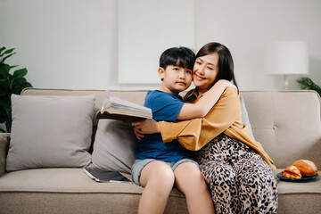 Happy asian mother and son sitting on family couch looking social media on smartphone with children hold laptop phone digital tablet having fun