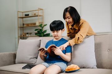 Happy asian mother and son sitting on family couch looking social media on smartphone with children...
