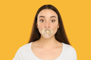 Beautiful young woman blowing bubble gum on yellow background