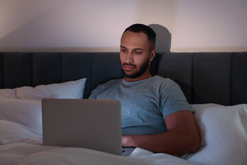 Young man using laptop in bed at night. Internet addiction