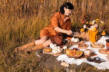 Fall picnic with pumpkin. Stylish woman enjoying autumn weather in the park. People, lifestyle, relaxation and vacations concept. Autumn harvest.