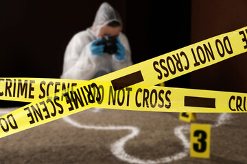 Yellow tapes blocking way to crime scene. Criminologist working indoors