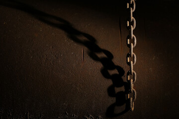 Hanging rusty scary chain hangs near the wall throwing a bent shadow on it