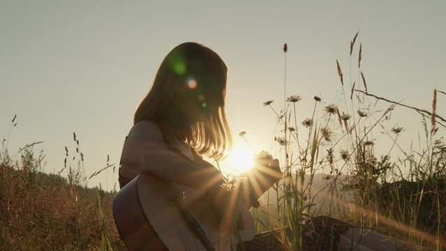 A young woman plays guitar against a beautiful backdrop wildflowers and sunsets, enjoying a moment musical creativity. Hobby with a guitar becomes even more enjoyable play among the blooming meadows