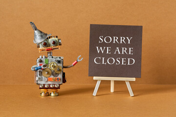 Sorry we are closed. A robot stands next to an easel and a brown poster with a warning inscription...