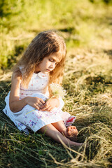 A cute little girl is playing on a sunny summer day in a blooming meadow. The child takes care of the flowers. The child has fun in nature.
