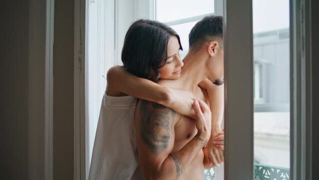 Cute newlyweds watching window at home close up. Love couple embracing indoors