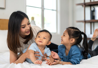 Portrait of enjoy happy love family asian mother playing with adorable little asian baby and sister girl, newborn, infant.Mom touching care with cute son in a white bedroom.Love of family concept - Powered by Adobe